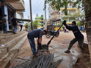 Bangalore, Karnataka, India-June 05 2021: Closeup of two indian young man wear mask and cutting the hexagon window rod manually in the road side during lockdown, covid 19 season