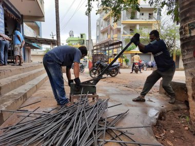 Bangalore, Karnataka, India-June 05 2021: Closeup of two indian young man wear mask and cutting the hexagon window rod manually in the road side during lockdown, covid 19 season