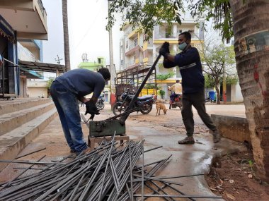 Bangalore, Karnataka, India-June 05 2021: Closeup of two indian young man wear mask and cutting the hexagon window rod manually in the road side during lockdown, covid 19 season