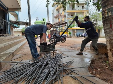 Bangalore, Karnataka, India-June 05 2021: Closeup of two indian young man wear mask and cutting the hexagon window rod manually in the road side during lockdown, covid 19 season