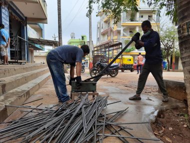 Bangalore, Karnataka, India-June 05 2021: Closeup of two indian young man wear mask and cutting the hexagon window rod manually in the road side during lockdown, covid 19 season