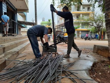 Bangalore, Karnataka, India-June 05 2021: Closeup of two indian young man wear mask and cutting the hexagon window rod manually in the road side during lockdown, covid 19 season