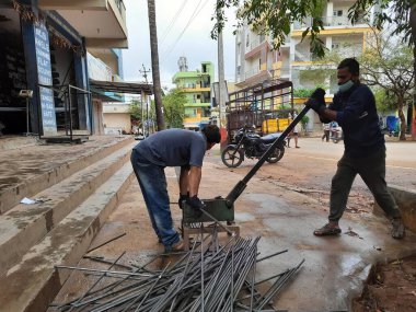 Bangalore, Karnataka, India-June 05 2021: Closeup of two indian young man wear mask and cutting the hexagon window rod manually in the road side during lockdown, covid 19 season