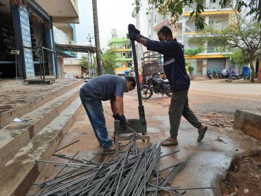 Bangalore, Karnataka, India-June 05 2021: Closeup of two indian young man wear mask and cutting the hexagon window rod manually in the road side during lockdown, covid 19 season