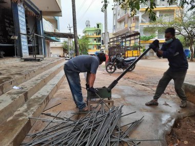 Bangalore, Karnataka, India-June 05 2021: Closeup of two indian young man wear mask and cutting the hexagon window rod manually in the road side during lockdown, covid 19 season