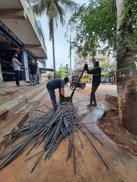 Bangalore, Karnataka, India-June 05 2021: Closeup of two indian young man wear mask and cutting the hexagon window rod manually in the road side during lockdown, covid 19 season