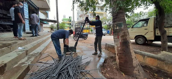 Bangalore, Karnataka, India-June 05 2021: Closeup of two indian young man wear mask and cutting the hexagon window rod manually in the road side during lockdown, covid 19 season