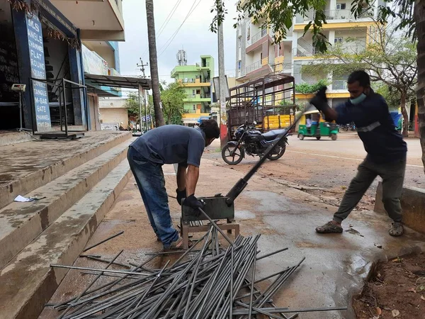 Bangalore, Karnataka, India-June 05 2021: Closeup of two indian young man wear mask and cutting the hexagon window rod manually in the road side during lockdown, covid 19 season