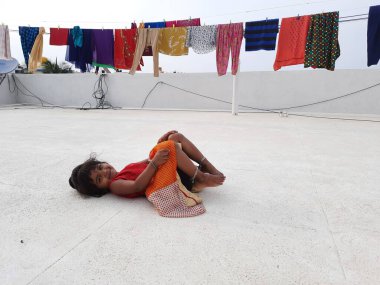 Bangalore, Karnataka, Hindistan-25 Nisan 2021: Kumaşların terasında oynayan Hintli genç kızın yakın çekimi gün ışığında kurumak üzere asılıyor.