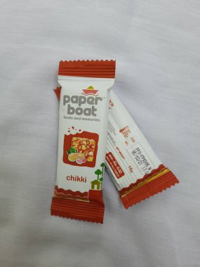 Bangalore, Karnataka, Hindistan-Aug 10-2021: Kağıt Teknesi Chikki veya Fıstık Çubuğu Paketinin Kapanışı Eklenmemiş Koruyucu ve Renkler beyaz arkaplanda izole edildi