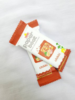 Bangalore, Karnataka, Hindistan-Aug 10-2021: Kağıt Teknesi Chikki veya Fıstık Çubuğu Paketinin Kapanışı Eklenmemiş Koruyucu ve Renkler beyaz arkaplanda izole edildi