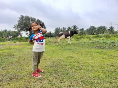 Channapatna, Karnataka, Hindistan-Aug 15 2021: Boş tarım alanında siyah beyaz renkli ineğin yanında duran Hintli çocuğun yakın çekimi.