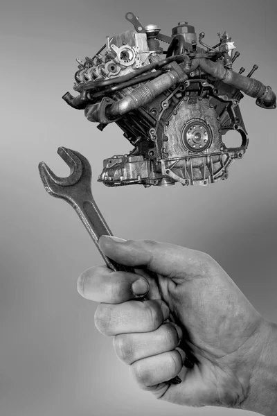 Schmutzige Hand hält Schraubenschlüssel und Motor des Autos isoliert auf grauem Hintergrund — Stockfoto