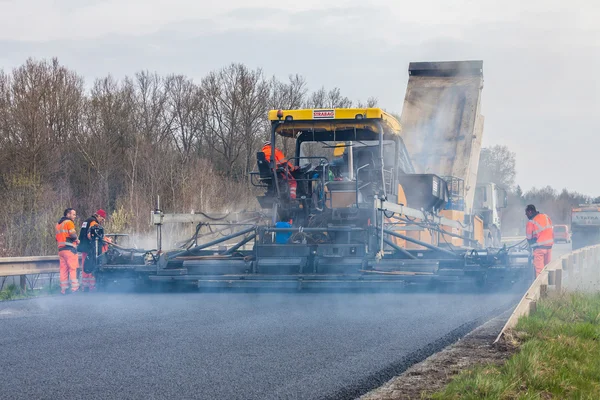 Trabalhador operando máquina de pavimentação de asfalto durante a construção e reparação de estradas — Fotografia de Stock