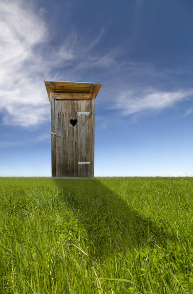 Wooden toilet, green field, blue sky