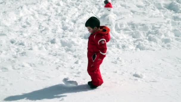 Малыш пинает снежок вместе со снеговиком — стоковое видео