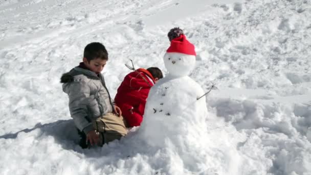 Dos hermanos jugando juntos con muñeco de nieve — Vídeos de Stock