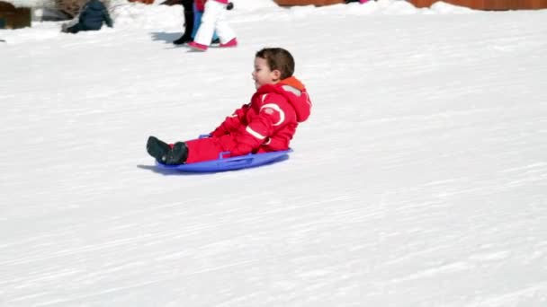 Niño feliz de cámara lenta que cae en la nieve con trineo — Vídeos de Stock