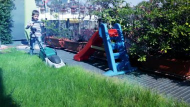 Çocuk bahçede çalışan çim biçme makinesi ile
