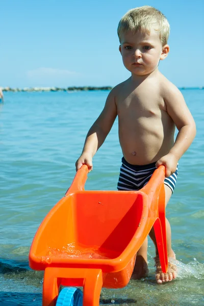 Criança com carrinho de mão transporta água do mar — Fotografia de Stock