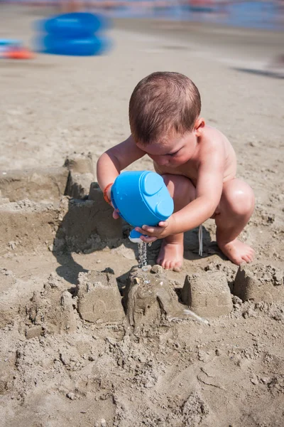 Pequeño niño jugando con la arena y la regadera en la playa italia mar — Foto de Stock