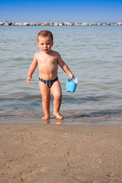 Menino brincando com areia e regando lata no mar itália praia — Fotografia de Stock