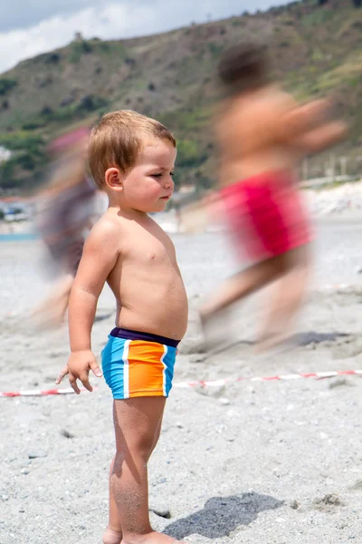Niño en la playa la gente en el fondo se mueve — Foto de Stock