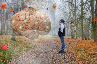 Dev insan beyninin önündeki sonbahar manzarasında duran bir adam. Beyin şu anda bilgi ve işlemleri iletiyor.