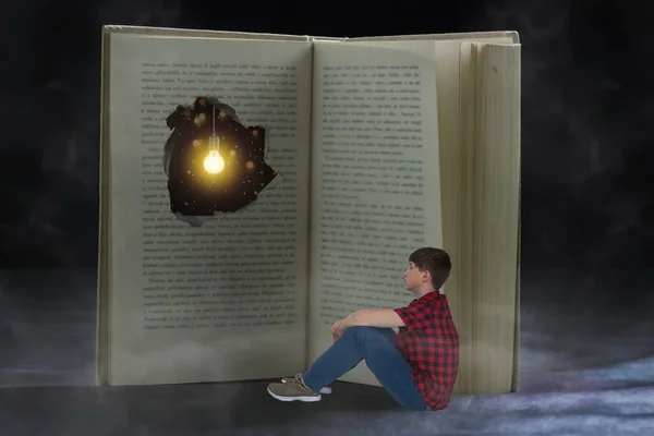 The boy is sitting in front of an old book with a hole in it and a light bulb hanging in it. The book is bigger than him. Celebrate Book Day.