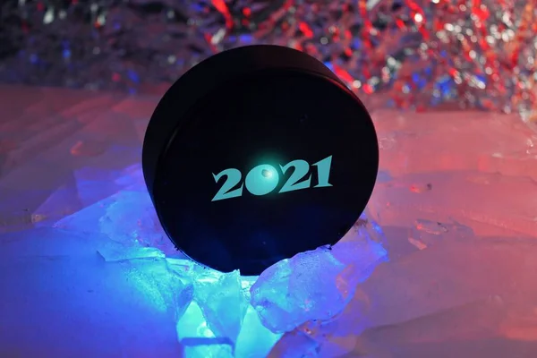 Hockey puck 2021 stands on the edge in cracked ice. A red-blue light falls on him. Czech hockey concept. The hockey puck broke the ice. Long live the World Hockey Championship in 2021.