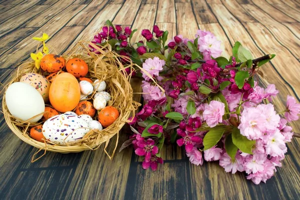 Bir sepette balmumu ve parıltıyla süslenmiş renkli yumurtalar ve süs kirazı dalları..