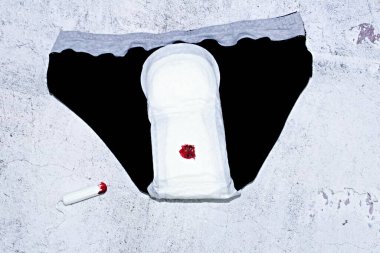 Adet yastıklı siyah külot ve bir damla kan ve kullanılmış tampon..