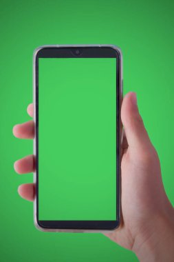 Mobile phone with a green screen in a male hand on a green background. Concept for mobile technology, communication and connection with the world.