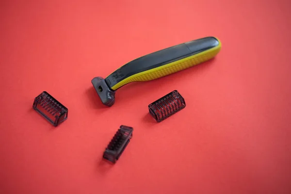 Beard trimmer with three attachments on the red background.