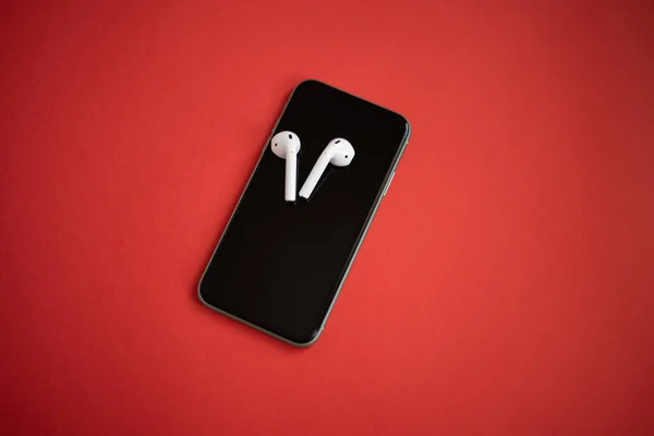 Karanlık bir arka planda iki kablosuz kulaklıklı modern bir telefon. Modern ve minimalist bir kavram. Metin için boşluk.