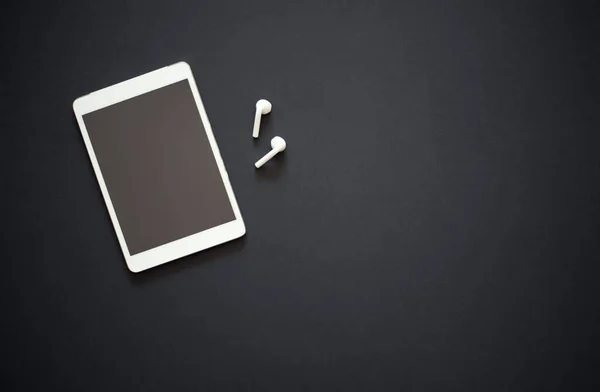 Siyah arka planda iki beyaz kablosuz kulaklığı olan modern bir tablet. Modern ve minimalist bir kavram. Metin için boşluk.