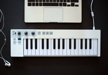 Müzisyenin işyeri. MIDI klavye, dizüstü bilgisayar ve siyah arka planda kablolu kulaklıklar. Düz yatıyordu.