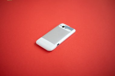 Kırmızı arka planda eski, modası geçmiş ve yıpranmış bir cep telefonu.