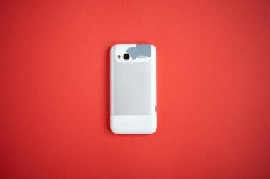 Kırmızı arka planda eski, modası geçmiş ve yıpranmış bir cep telefonu.