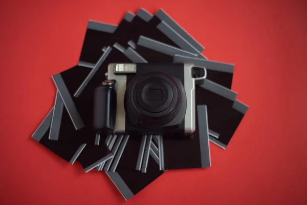A modern instant print camera and a stack of photo cards for printing on a red background.