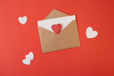 İçinde beyaz notlar olan bir zarf ve kırmızı arka planda sevgililer günü kalpleri. Düz yerde, üst tarafta. Sevgililer Günü konsepti için romantik aşk mektubu.