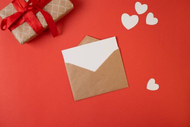 İçinde beyaz notlar olan bir zarf ve kırmızı arka planda sevgililer günü kalpleri. Düz yerde, üst tarafta. Sevgililer Günü konsepti için romantik aşk mektubu.