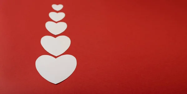 Kırmızı arka planda kağıt kalpler var. Kağıt kesiği şekilli soyut bir arkaplan. Aziz Valentine, Anneler Günü, doğum günü tebrik kartları, davetiye, kutlama konsepti.