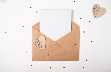 Zarfın içinde boş bir kağıt ve beyaz arka planda tahta bir kalp var. Sevgililer Günü konsepti için romantik aşk mektubu. Metin için boşluk.