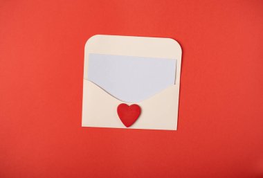 Kırmızı arka planda kırmızı ahşap bir kalp olan bir zarf. Düz konum, üst görünüm, metin için boşluk. Sevgililer Günü konsepti için romantik aşk mektubu.