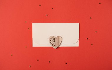 Kırmızı arka planda zarf ve ahşap kalp. Düz yatıyordu. Sevgililer Günü konsepti için romantik aşk mektubu.