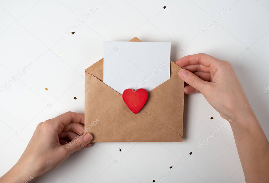 Woman's hands holding a letter in craft envelope on the white background. Valentine's day concept. Space for text.