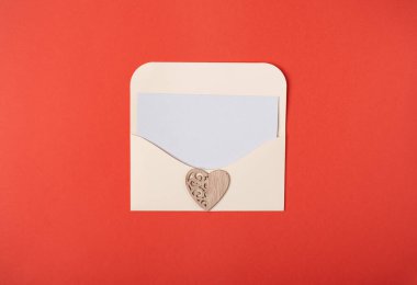 Zarfın içinde boş bir kağıt ve kırmızı arka planda tahta kalpler var. Sevgililer Günü konsepti için romantik aşk mektubu. Metin için boşluk.