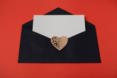 İçinde boş bir kağıt olan siyah bir zarf ve kırmızı arka planda tahta bir kalp. Sevgililer Günü konsepti için romantik aşk mektubu. Metin için boşluk.