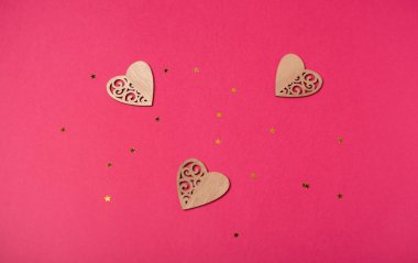Üç tahta kalp ve pembe arka planda küçük altın yıldızlar. Sevgililer Günü konsepti. Düz yatış, üst görünüm.